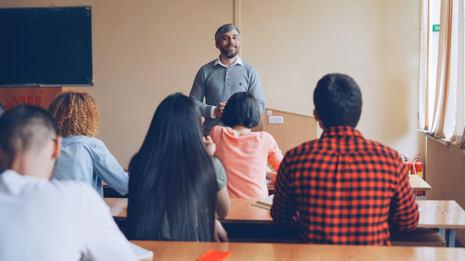 Sala de aula com alunos adolescentes sentados em carteiras, sem celulares à vista