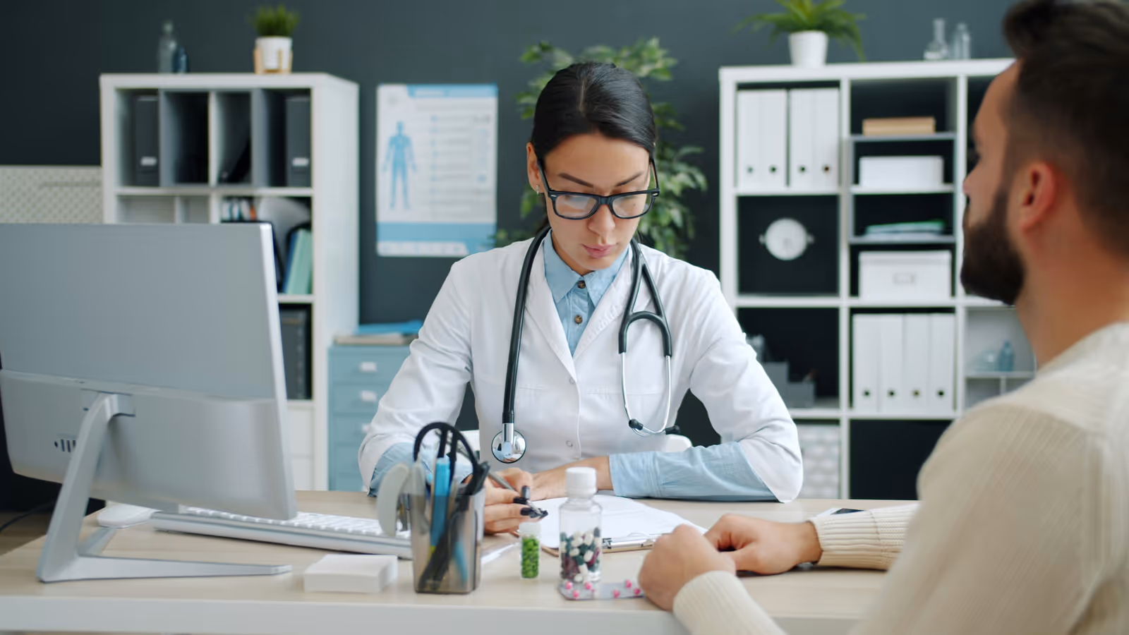 Médica conversando com paciente em consultório, anotando no prontuário, documentação clínica em foco