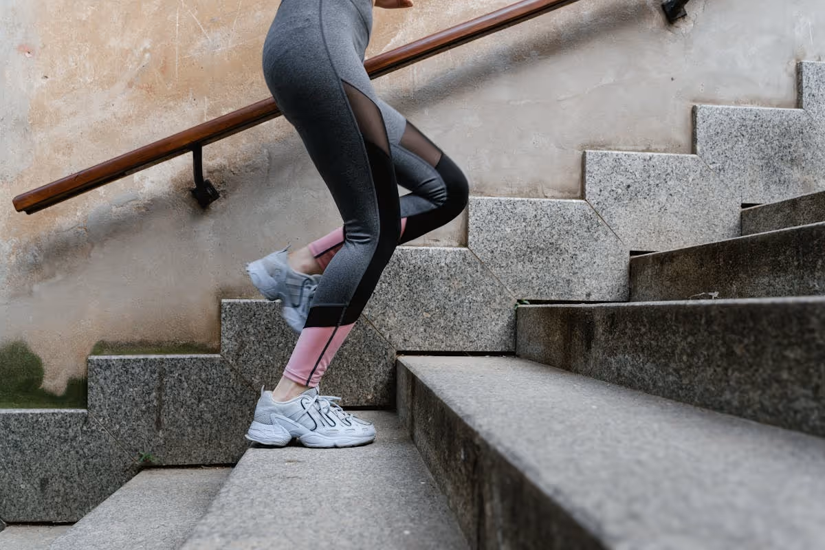 Mulher com roupa esportiva subindo escada de concreto ao ar livre