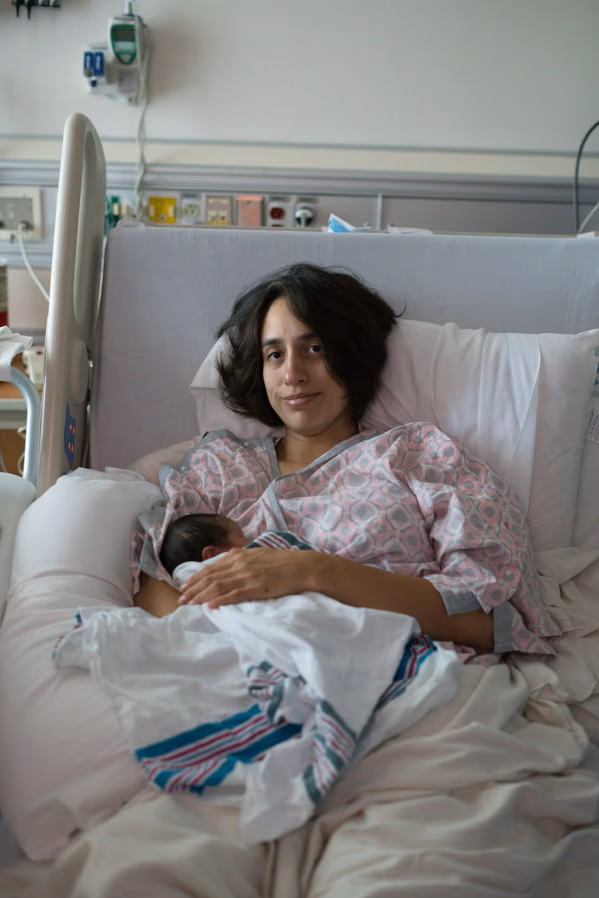 Mãe segurando bebê recém-nascido em leito hospitalar, luz quente