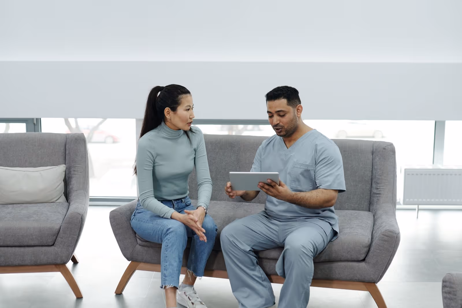 Profissional de saúde mostra informações em um tablet a uma paciente sentada em uma clínica