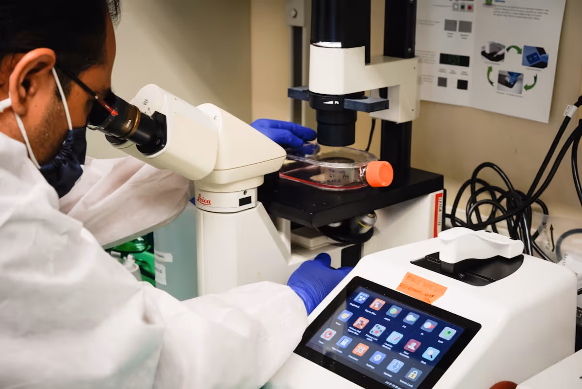 Pesquisador com jaleco e luvas examina amostra em microscópio invertido em laboratório de pesquisa