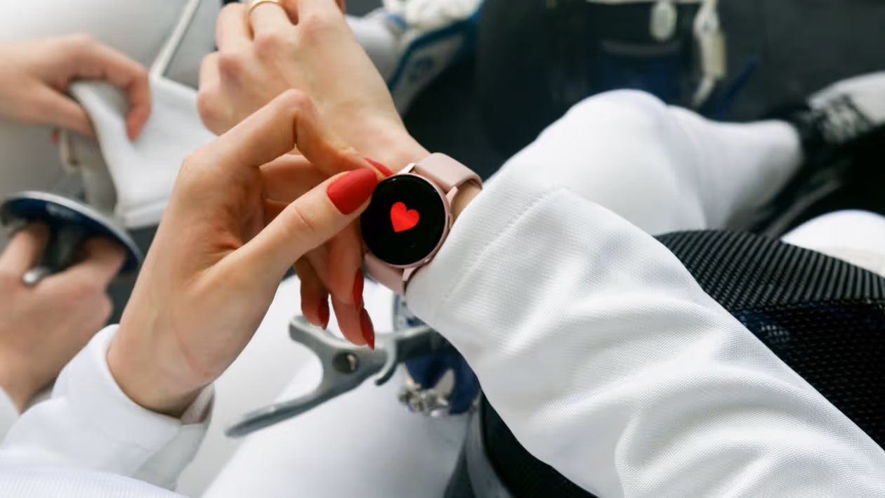 Mão de mulher com unhas vermelhas interagindo com smartwatch que exibe ícone de coração